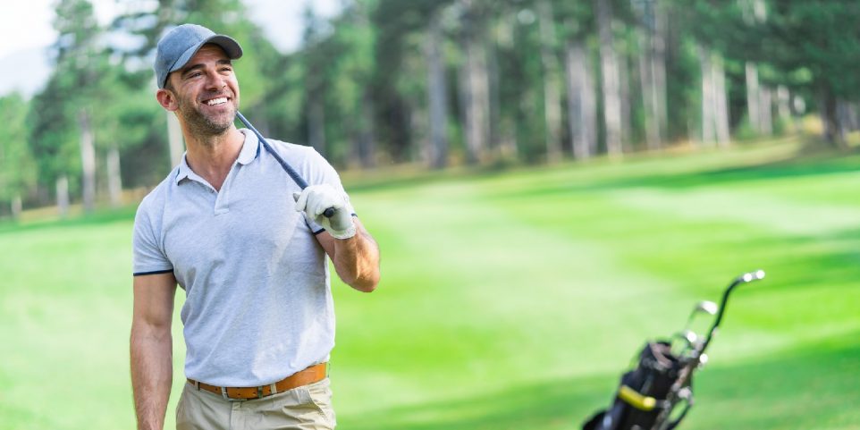 Adult golf player standing leisurely on the golf course and looking away to the goal