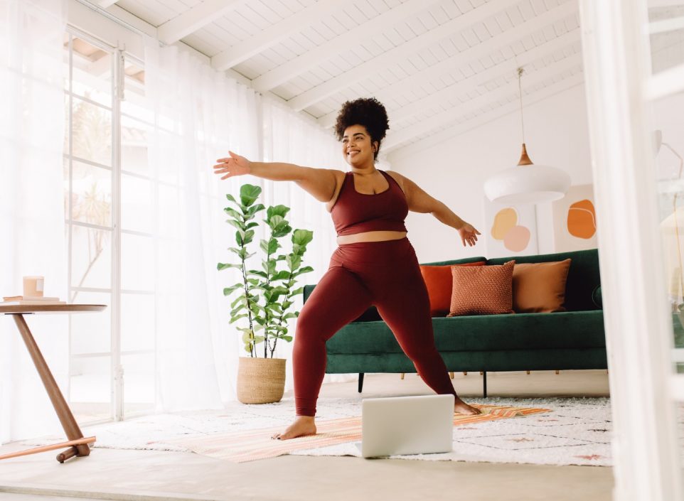 Full length of plus size woman stretching at home.