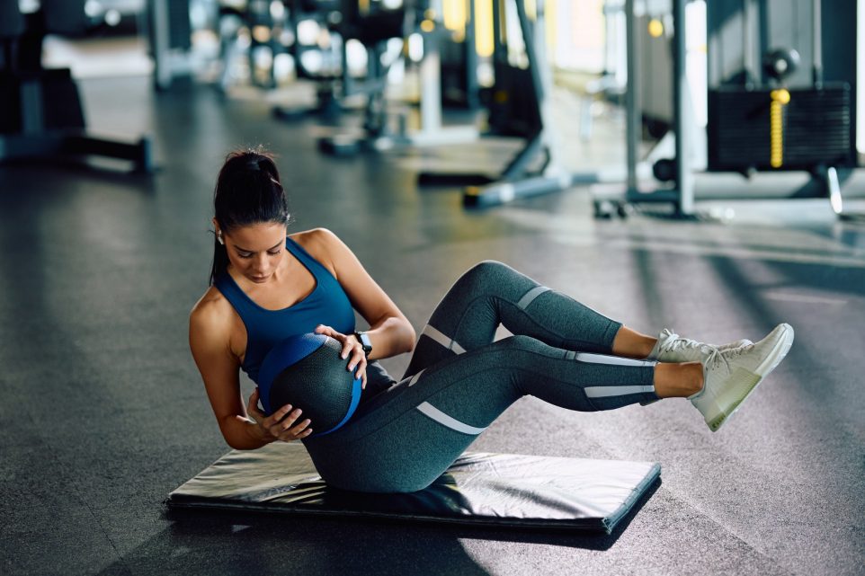 Athletic woman using medicine ball while doing sit-ups during sports training in a gym.