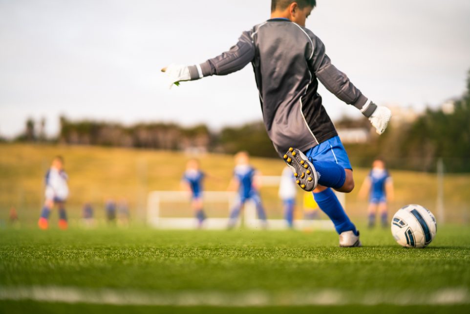 Little soccer player in soccer field playing soccer outdoor in casual clothing.