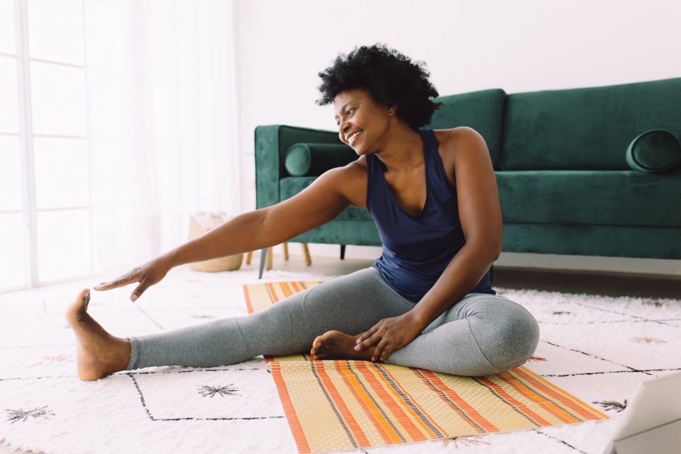 African woman doing stretching at home. Mature woman at home keeping fit by exercising.